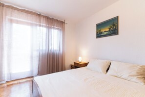 A hotel room with a bed, a nightstand with a lamp, a painting on the wall, and a window with curtains.