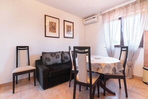 A living room with a sofa, two chairs, a dining table, and two framed pictures on the wall.