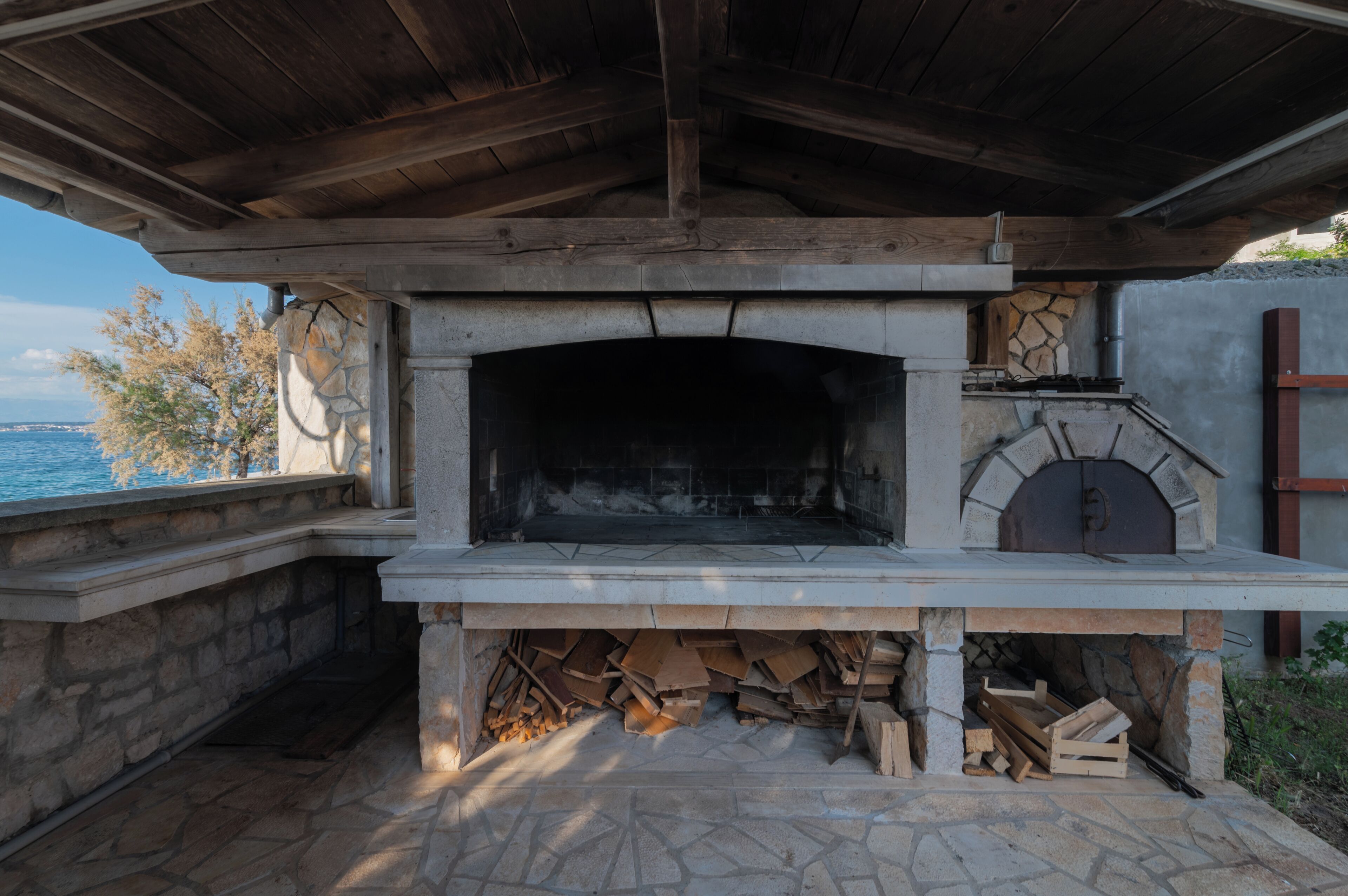 An outdoor stone fireplace with a chimney, a stone bench, and a view of the sea.