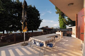 An outdoor patio with a table and chairs, a flag, and a view of the water and trees. - Beachfront Studio-apartment Spazzio (Preko)