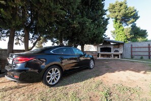 A black car parked in a driveway with a stone building and a large tree in the background. - Beachfront Studio-apartment Spazzio (Preko)