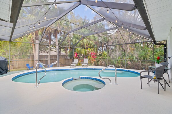 Une piscine intérieure avec un jacuzzi, entourée de chaises longues et d’un patio couvert.