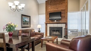 A dining area with a wooden table and chairs, a vase of flowers, a fireplace, and a television mounted on the wall.