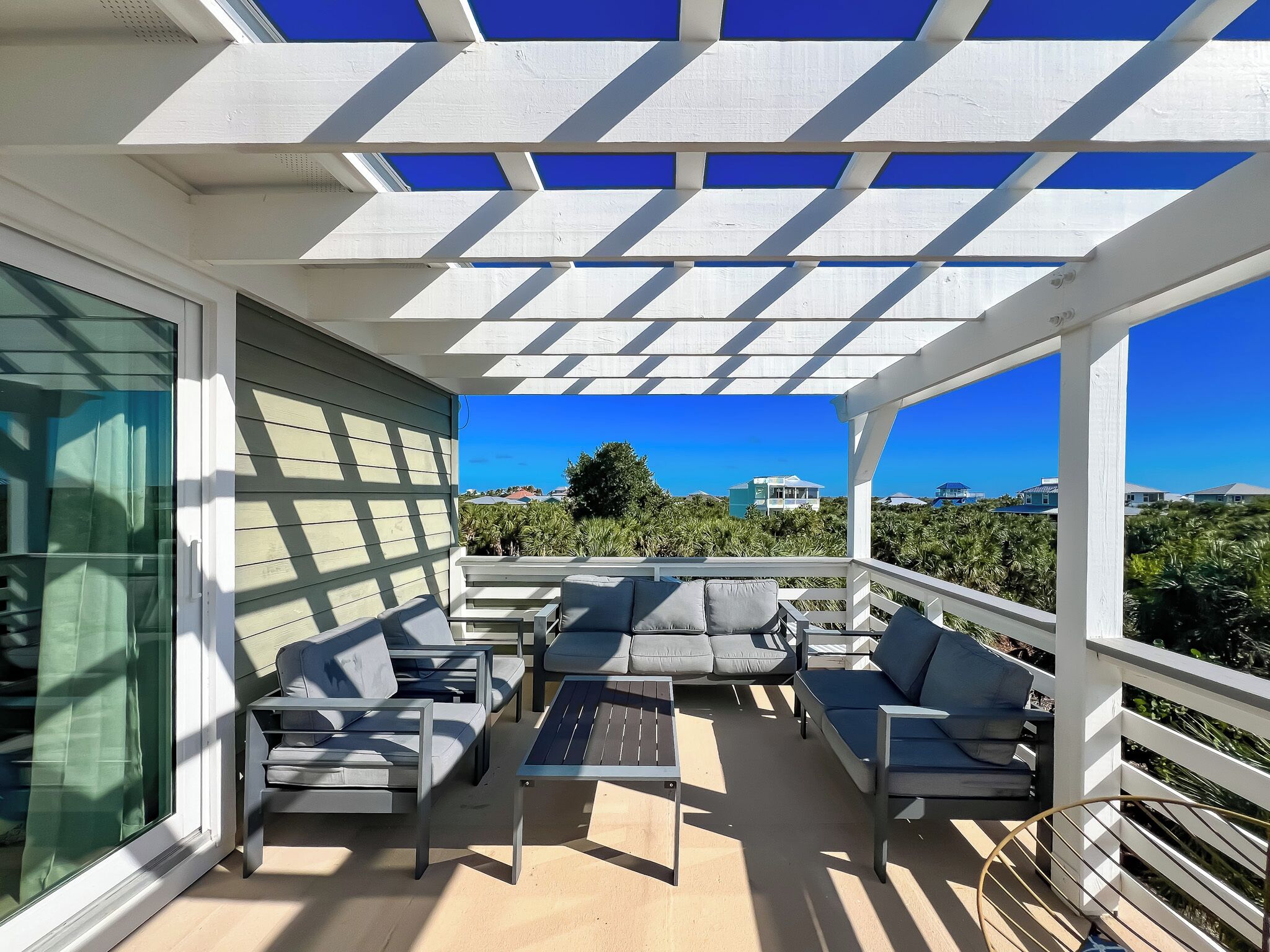 A covered outdoor seating area with a view of the ocean and neighboring houses.