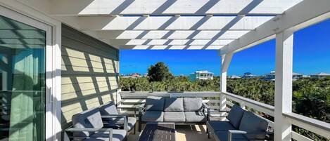 A covered outdoor seating area with a view of the ocean and neighboring houses.