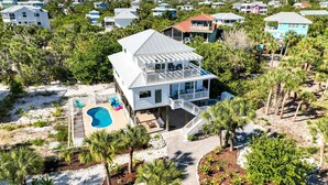 Una casa grande con piscina, rodeada de palmeras y vista a la playa.
