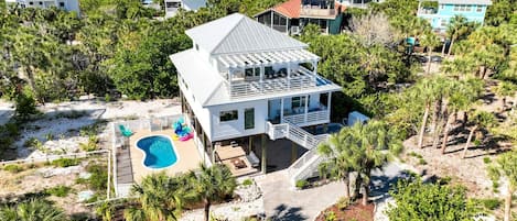 Una casa grande con piscina, rodeada de palmeras y vista a la playa.