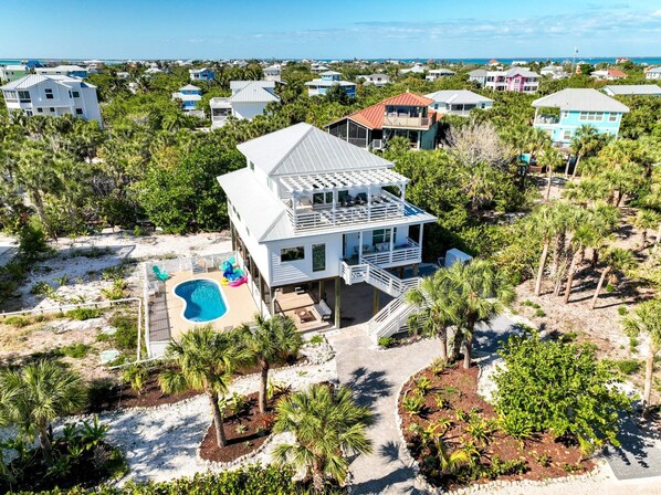 Una casa grande con piscina, rodeada de palmeras y vista a la playa.