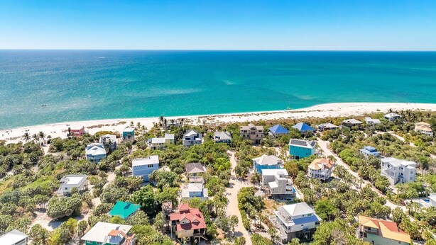 Vista aérea de una zona residencial costera con casas, cielos azules despejados y una playa.