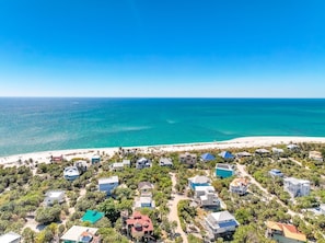 Vista aérea de una zona residencial costera con casas, cielos azules despejados y una playa.