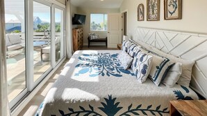 Un dormitorio con cama, ventilador de techo, televisión y balcón con vistas.