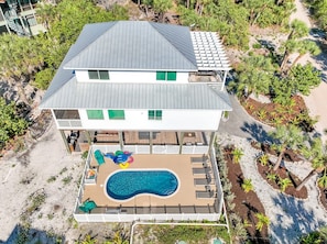 Una casa de dos pisos con piscina, rodeada de vegetación tropical.