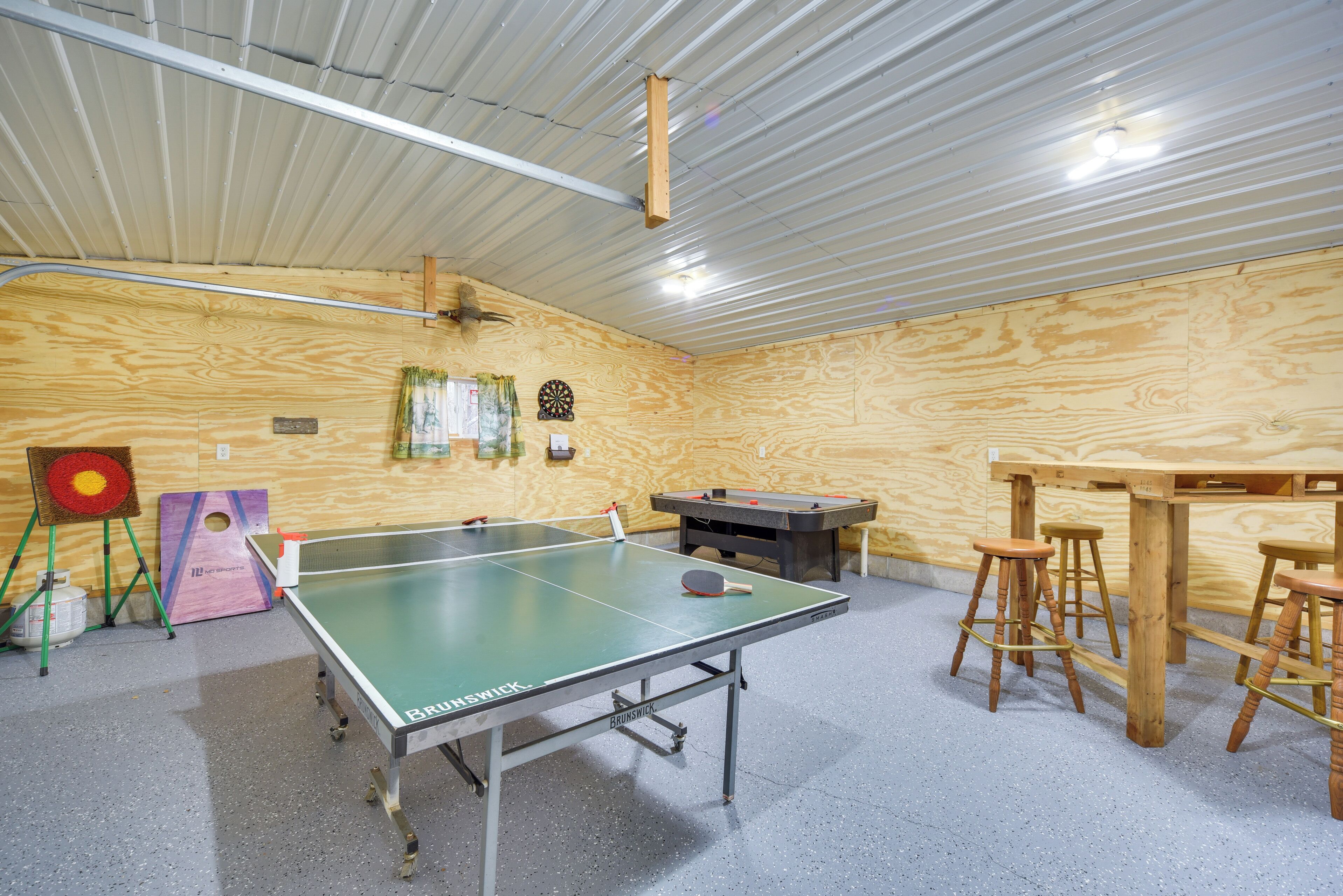 Een tafeltennistafel met krukken, een dartbord en nog een dartbord in een kamer met houten wanden en een metalen plafond.