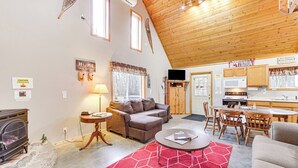 Ein gemütliches Wohnzimmer mit Kamin, einer Couch, einem Couchtisch und einem roten Teppich. Es gibt eine Küchenzeile mit Holzschränken und einer Mikrowelle.