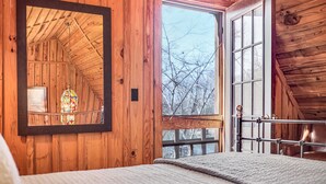 Habitación de cabaña de madera con una ventana grande, una cama y un espejo que refleja el cuarto.