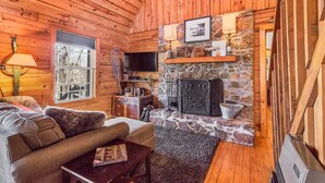 Interior acogedor de una cabaña con chimenea de piedra, paredes de madera, un sofá y un televisor.