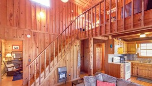 Interior de una cabaña de madera con escalera, sala de estar, cocina y un pequeño comedor.