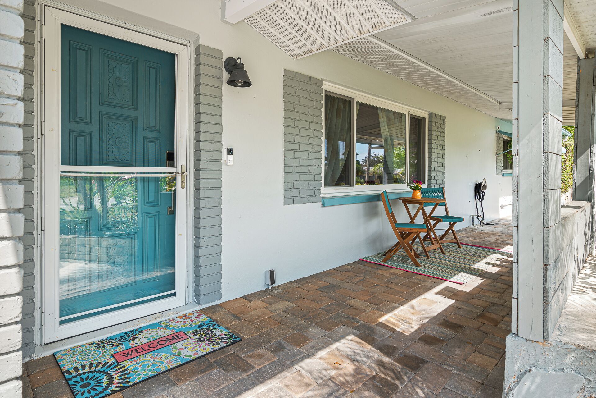 A covered porch with a teal door, a bench, and a small table with a vase.