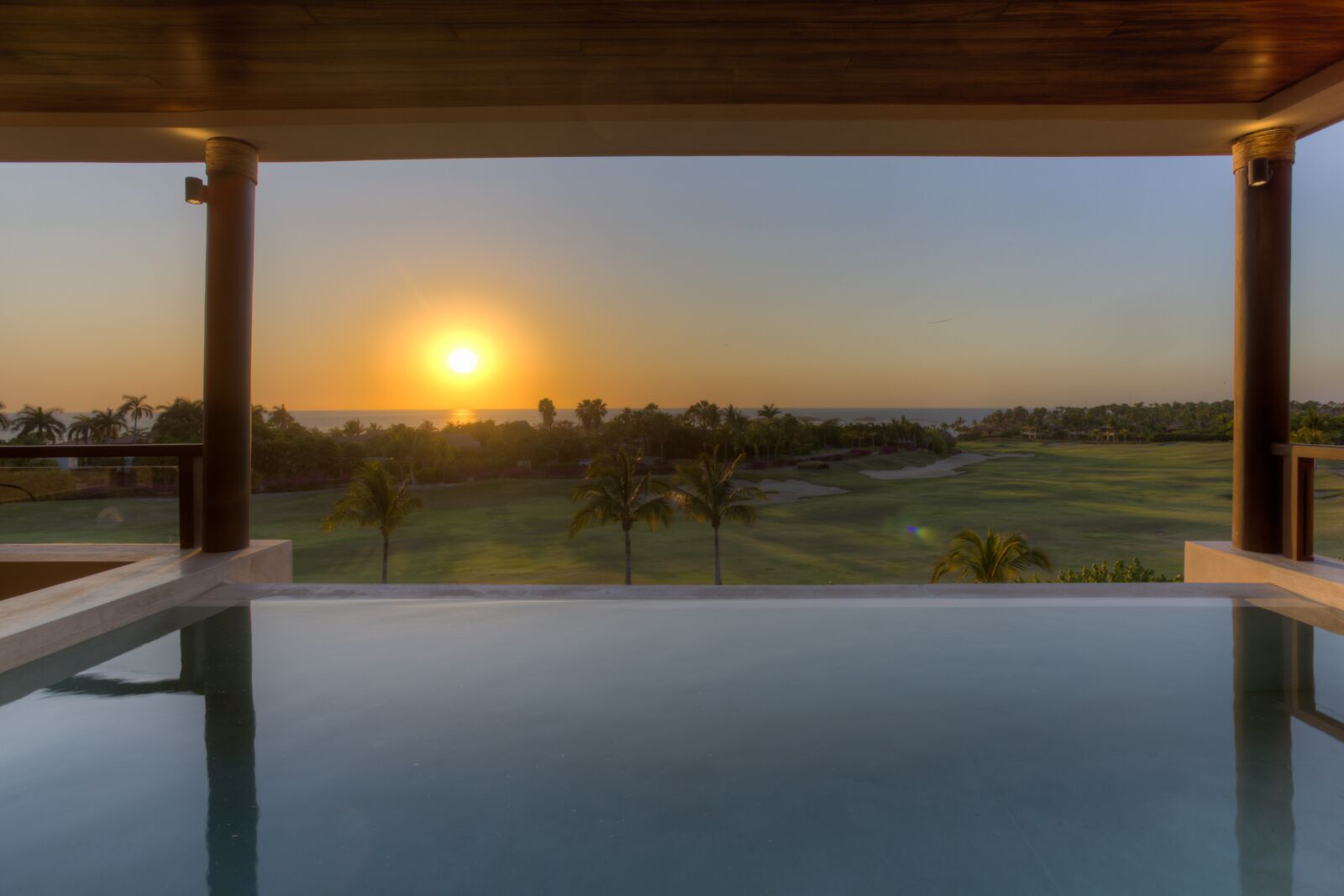 A pool area with a view of a golf course and palm trees at sunset.