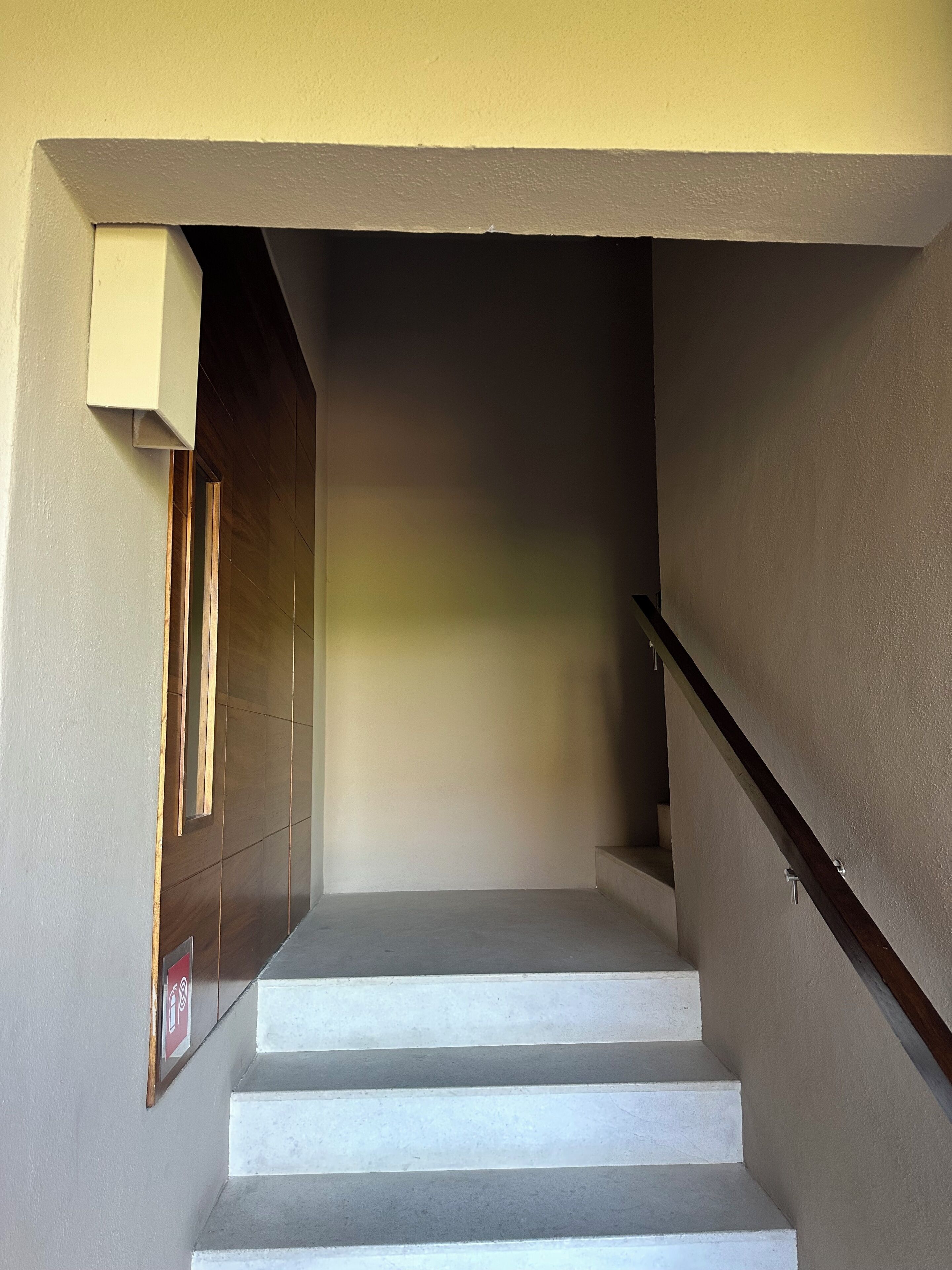 Eine Treppe mit Handlauf, eine Tür mit Fenster und eine Wand mit einem Schild.