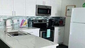 A modern kitchen with white cabinetry, a stainless steel microwave, a built-in oven, and a white refrigerator. - New! Lakefront 2-bedroom Condo. Newly remodeled. (Willis)