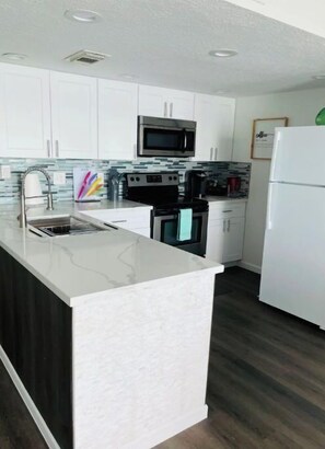 Kitchen features a central island with a sink and stovetop, surrounded by white cabinetry and a microwave above.