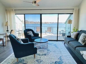 Relax in this stylish living room with a balcony overlooking a serene body of water.
