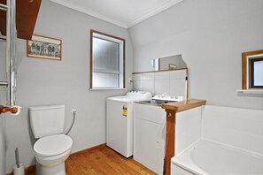 A compact bathroom with a toilet, a washing machine, and a bathtub. - Snow Chalet - Fairlie Holiday Home (Fairlie)
