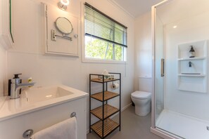 Un baño moderno con lavamanos blanco, espejo, inodoro y cabina de ducha de vidrio.