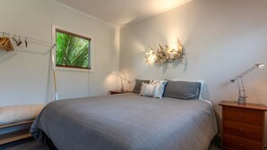 Un dormitorio con una cama grande, una mesita de noche, un aparador, una ventana con vistas a zonas verdes e iluminación en la pared.