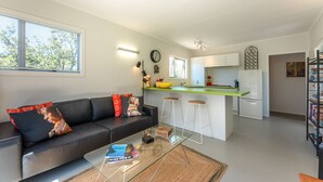 Un espacio de estar moderno con un sofá, una mesa de centro y una cocina que incluye un refrigerador, taburetes de bar y una encimera.