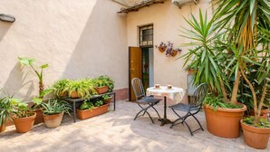 Un patio exterior con plantas en macetas, una mesa con sillas y una unidad de aire acondicionado en la pared.