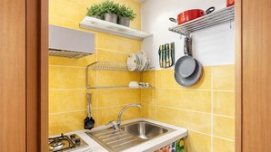 Una cocina con baldosas amarillas, un fregadero de acero inoxidable, una estufa a gas y estantes con utensilios y utensilios de cocina.