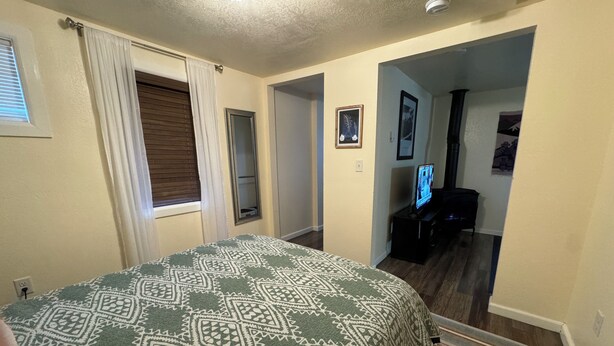 A bedroom with a patterned bedspread, a window with curtains, a door, and a hallway leading to another room. - Centrally located 1 bd/1ba bungalow (Missoula)