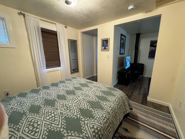 A bedroom with a patterned bedspread, a window with curtains, a door, and a hallway leading to another room.