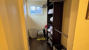 A narrow hallway with wooden flooring, a closet with hanging clothes, a laundry basket, and a window with blinds. - Centrally located 1 bd/1ba bungalow (Missoula)