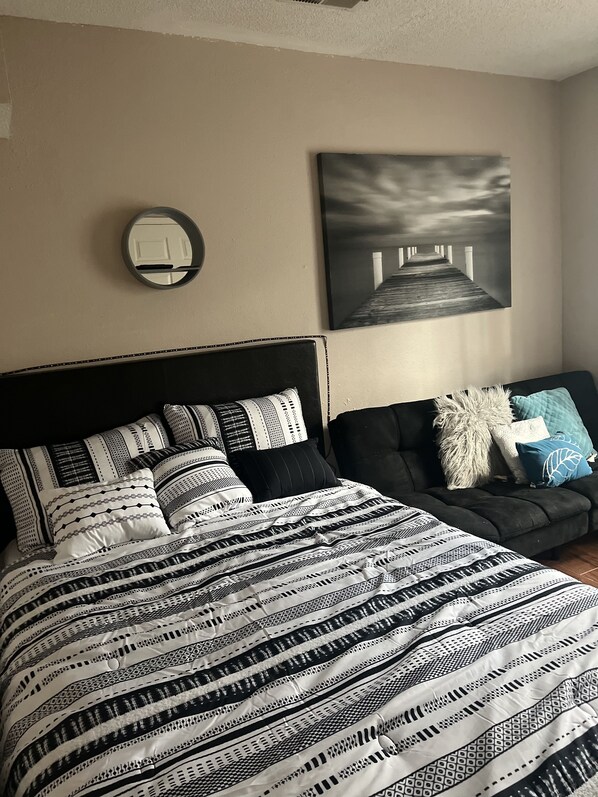 A bedroom with a large bed, a sofa, a wall-mounted mirror, and a painting of a pier.