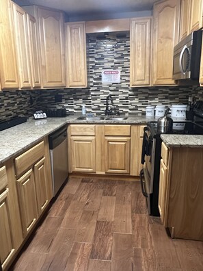 A kitchen with wooden cabinets, a granite countertop, a stainless steel sink, and a tiled backsplash.