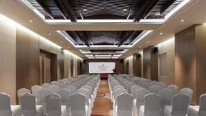A conference room with rows of white chairs, a stage with a screen displaying 'RAMADA', and a modern ceiling design. - Ramada by Wyndham Daocheng (Garze)