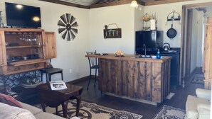 Een gezellige woonkamer met een houten salontafel, een bank en een televisie. Er is een keukenhoek met een fornuis en een spoelbak.