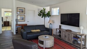Ein modernes Wohnzimmer mit einem schwarzen Ledersofa, einem runden Couchtisch, einem Fernseher und einer Holzkommode.