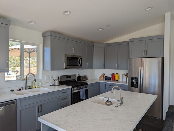 A modern kitchen with grey cabinets, stainless steel appliances, a large island with a sink, and a window providing a view of the outdoors.