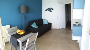 En moderne stue med en sort sofa, et spisebord med stole, en lampe og et kunstværk på væggen.
