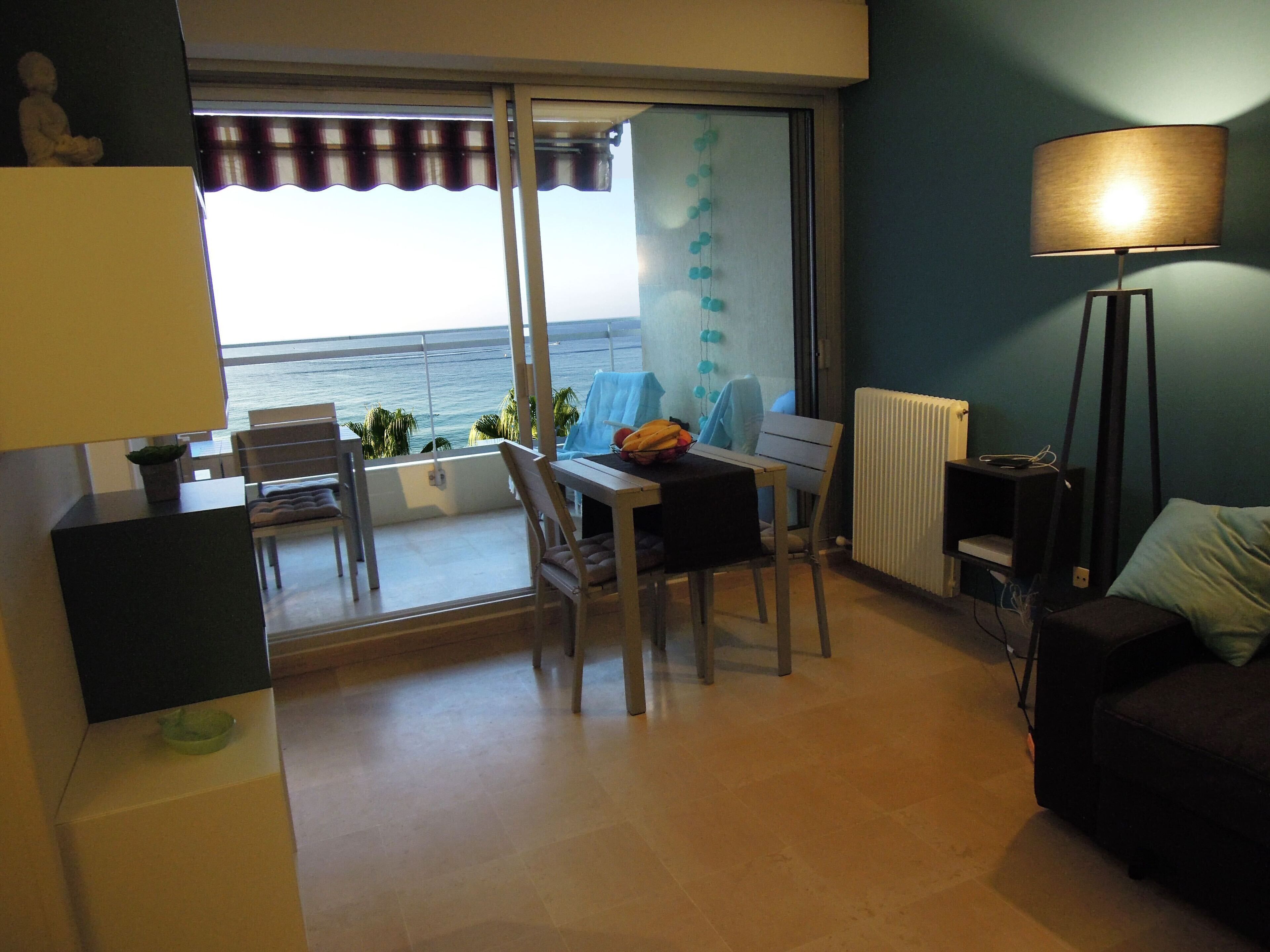 A balcony with a view of the sea, a dining table with chairs, a sofa, and a lamp.