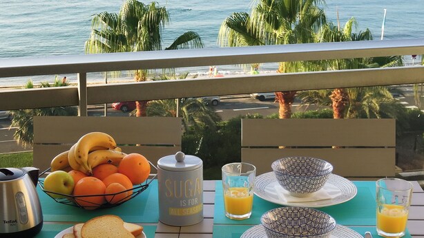 Et morgenbord med frugt, juice og en sukkerdåse, med udsigt til en strand.