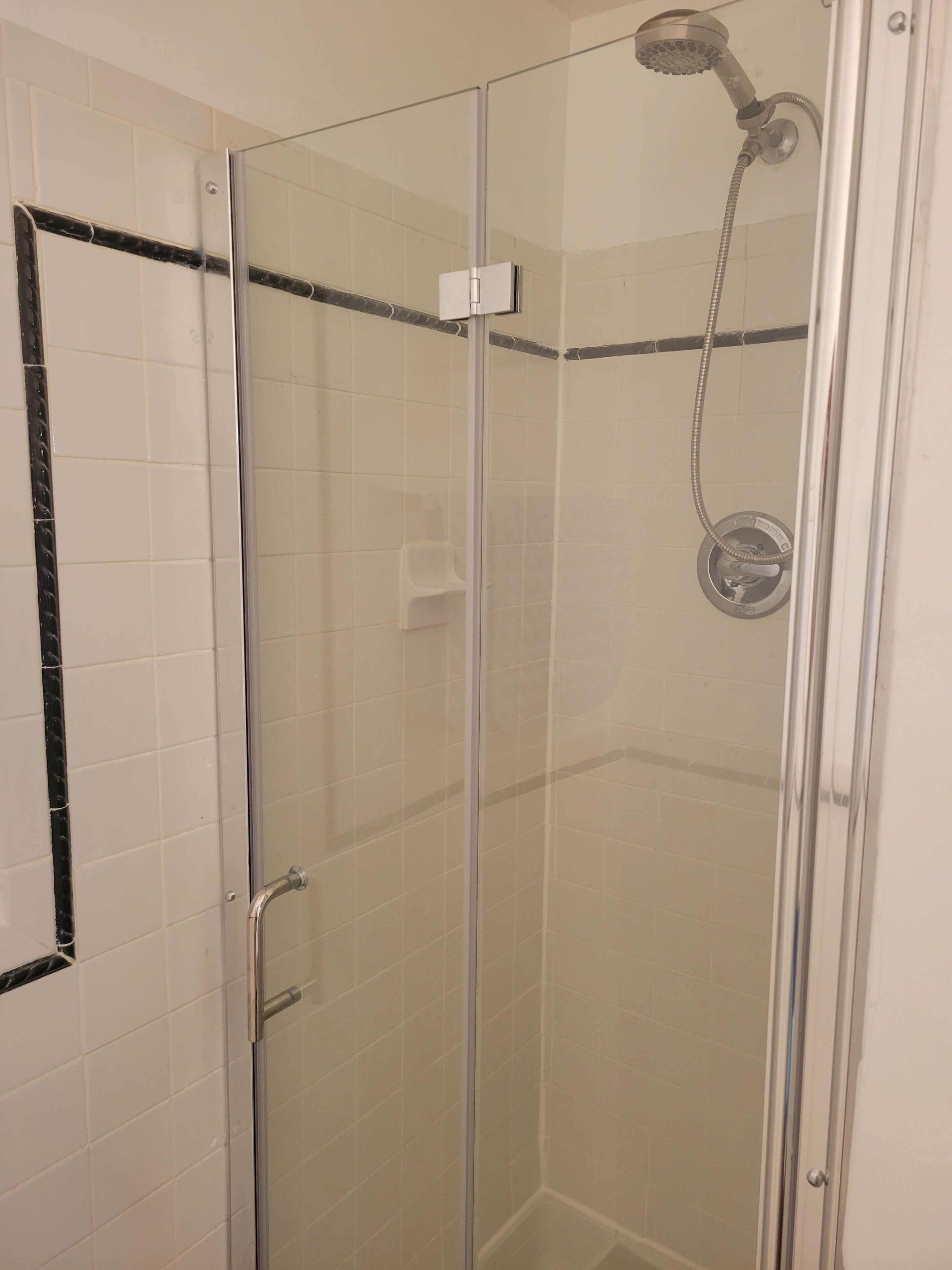 Une cabine de douche fermée par des parois en verre, dotée d’un pommeau de douche à main et d’un panneau de commande fixé au mur.