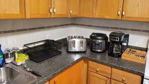 Una cocina con gabinetes de madera, encimera de granito, un tostador, una cafetera y un escurreplatos.