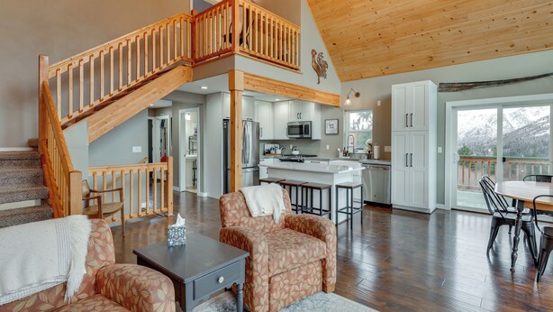 A spacious living area with a wooden staircase, a kitchen with modern appliances, and a dining area with a view of the mountains. - Stunning Alaskan Getaway w/ River & Mtn Views (Eagle River)