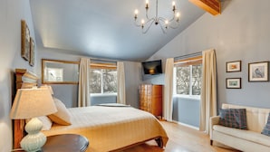 A bedroom with a bed, bedside table, lamp, dresser, TV, and a sofa. - Stunning Alaskan Getaway w/ River & Mtn Views (Eagle River)