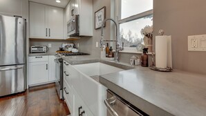 A modern kitchen with stainless steel appliances, white cabinetry, a large window, and a view of the outdoors. - Stunning Alaskan Getaway w/ River & Mtn Views (Eagle River)